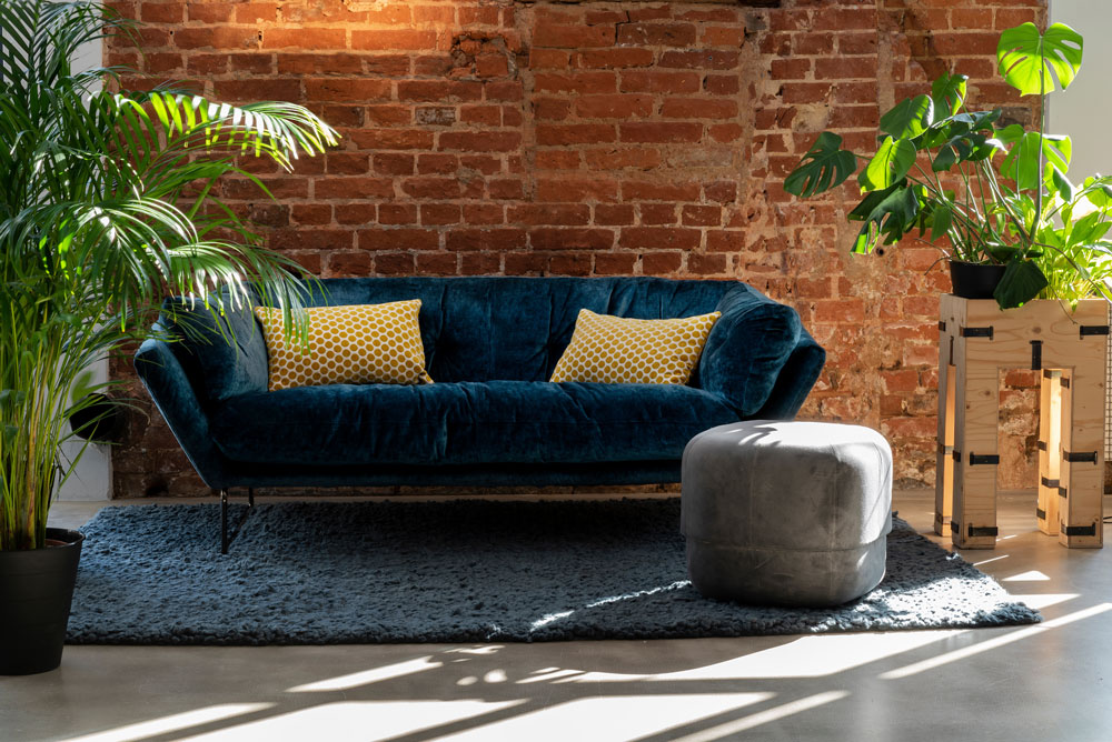 loft space with blue velvet sofa, brick wall and house plants